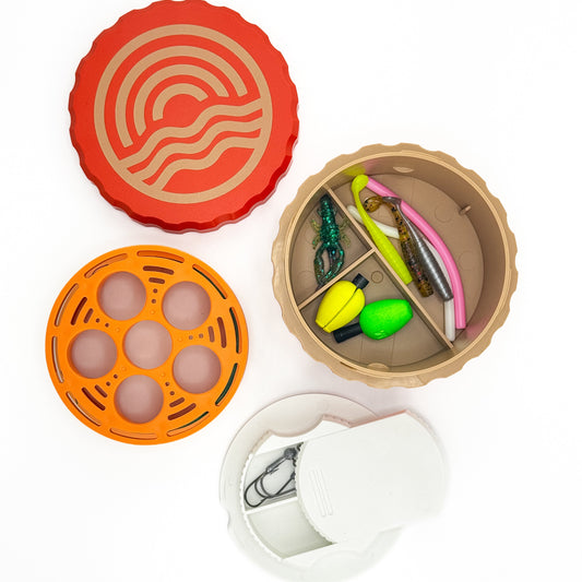 Set of fishing lures in a box with a red lid, orange egg-shaped container, and white container.