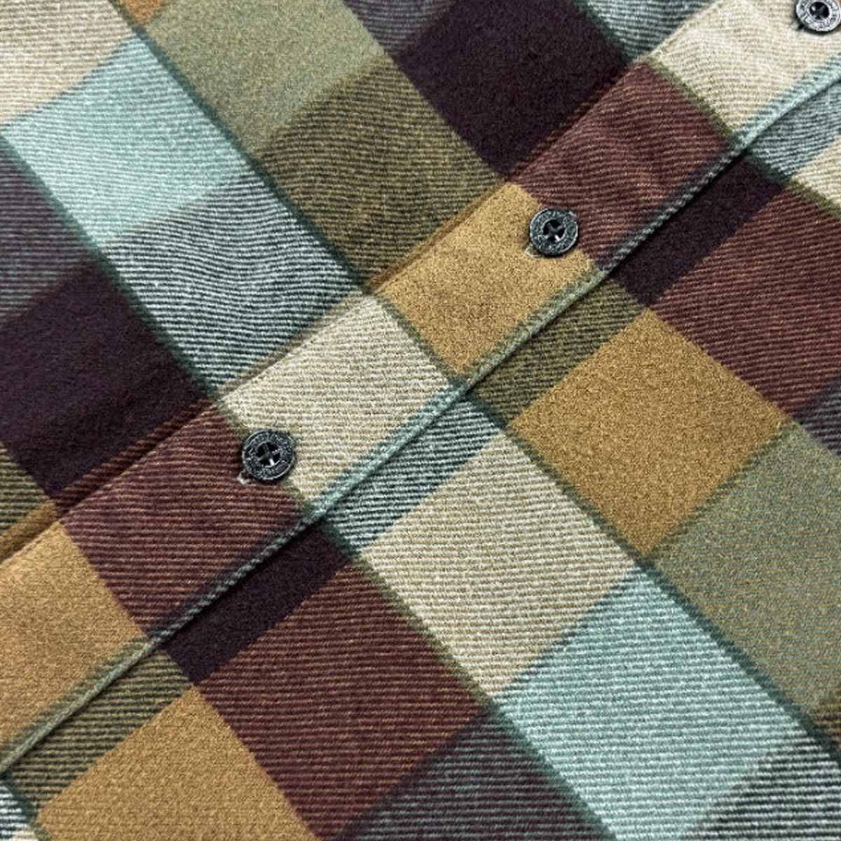 A close-up of a plaid fabric pattern with intersecting bands of muted green, tan, burgundy, and cream, showing the woven texture and a buttoned collar detail.