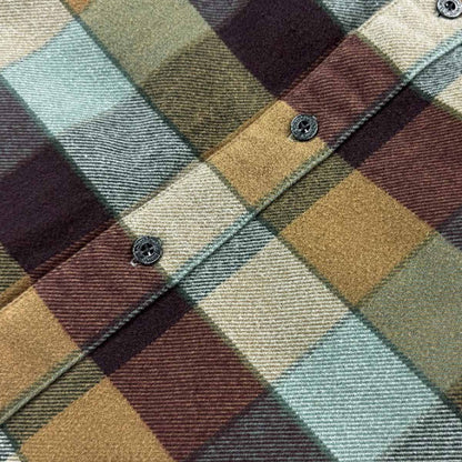A close-up of a plaid fabric pattern with intersecting bands of muted green, tan, burgundy, and cream, showing the woven texture and a buttoned collar detail.